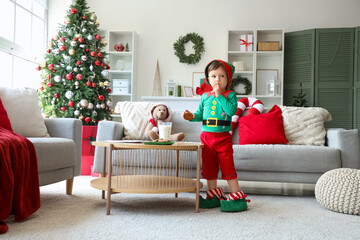 Sticker - Cute little boy in elf costume with cookies showing silence gesture at home on Christmas eve