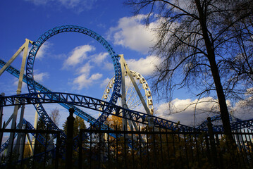 Roller coaster, carousel in an amusement park in autumn against the blue sky with clouds, amusement park, roller coaster.