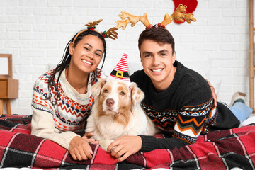 Poster - Happy young couple with dog lying in bedroom on Christmas eve