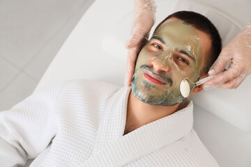 Canvas Print - Beautician applying cosmetic gel mask on handsome man's face and doing massage with roller in spa salon