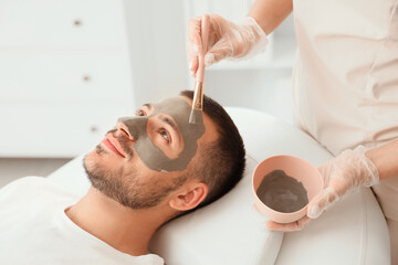 Canvas Print - Beautician applying cosmetic clay mask on handsome man's face in spa salon