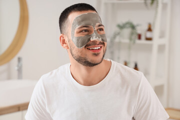 Canvas Print - Handsome young happy man with cosmetic clay mask on face in bathroom at home