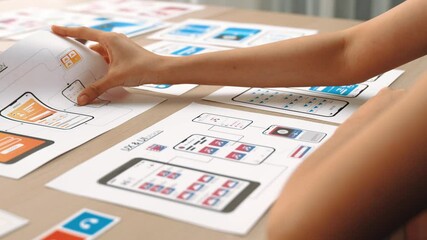 Startup company employee planning for user interface prototype for mobile application or website in office with model of program on desk. UX UI designer consider user friendly interface plan. Synergic