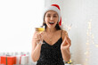 © Pixel-Shot - Beautiful young woman in Santa hat with Christmas sparkler and glass of champagne in living room