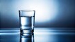 © Indigo Studio - A simple glass of clear liquid reflecting on a blue surface with soft lighting from above.