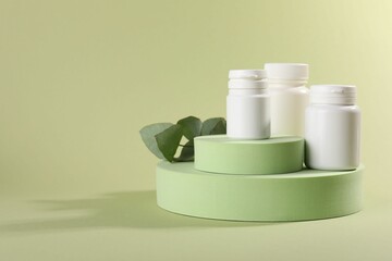 Wall Mural - Plastic medical bottles, leaves and podiums on green background, space for text