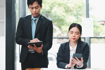 Wall Mural - Two business professionals in formal attire working together using digital devices in a modern office setting.