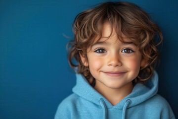 portrait of a cheerful young boy in a blue hoodie against a vibrant blue background exuding innocence and happiness his bright smile captures the essence of childhood joy and the simplicity of youth