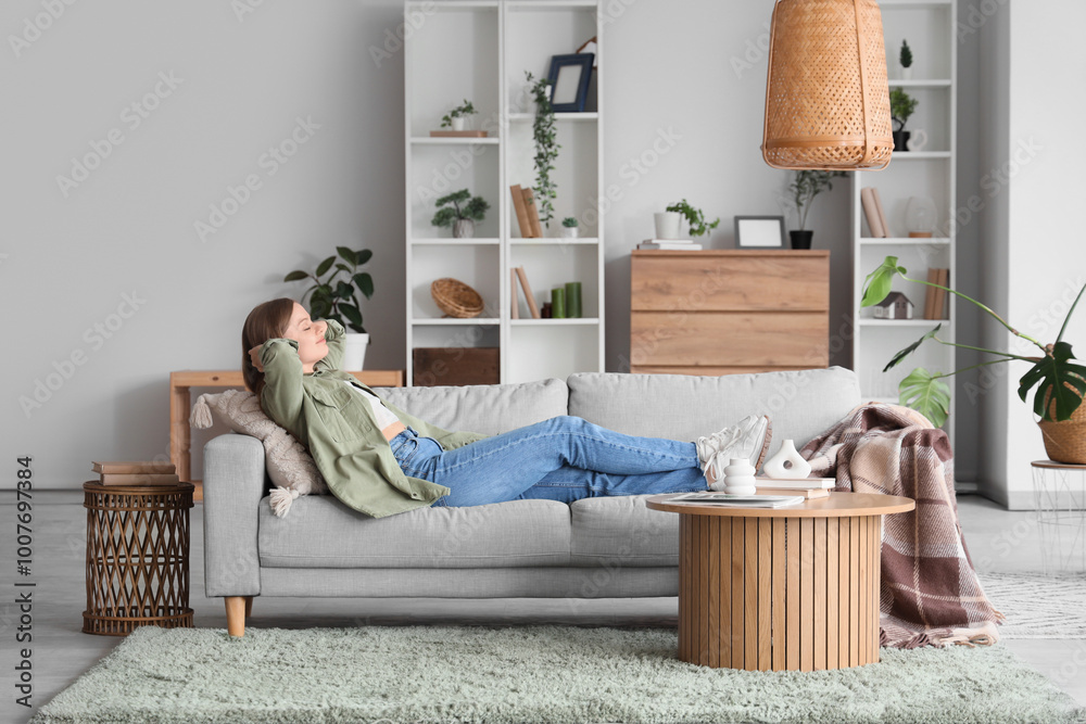 Young woman lying on grey sofa in light living room