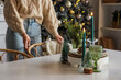 © Pixel-Shot - Burning candles with Christmas decor on dining table against woman at home, closeup