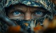 © Lexyat - Close-up of a man's intense blue eyes peering from beneath a camouflage hood.