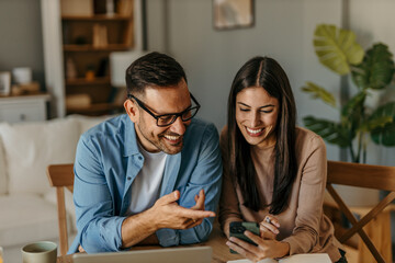 A couple in love is sitting together at a table, using a laptop and a payment card, while both are looking at products on the screen