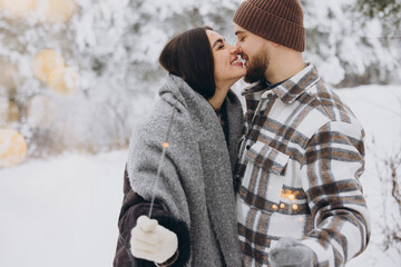 Wall Mural - Happy romantic couple in love holding sparklers in snowy winter forest