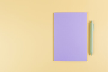 Wall Mural - Top view of purple notebook, green pen on yellow background. School, office wallpaper. Flat lay, copy space.