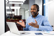 © Liubomir - Smiling professional man using laptop for video conference call. Wearing headset, actively participating in meeting. Modern office setting suggests business environment with efficient communication.