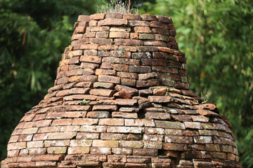 The top section of an ancient stupa, showcasing intricately layered bricks with natural moss and greenery peeking through, reflecting the beauty of historical architecture