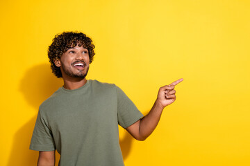 Wall Mural - Photo of positive guy with curly hairstyle dressed khaki shirt indicating look at logo empty space isolated on yellow color background