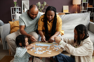 family gathered around wooden table solving puzzle, focusing on pieces and working together. living 