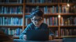 © TENGKUIZAHAM - Young boy is using a laptop in a library, surrounded by shelves full of books