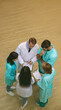 © My Ocean studio - An overhead shot of a medical team, including a senior doctor and four healthcare professionals, discussing patient notes. All wear scrubs or lab coats in a clinical setting.