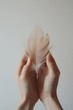 © Fokasu Art - Two hands softly cradling a tiny bird feather on a white background, with space for text, lightness and fragility