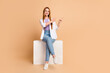 © deagreez - Full length photo of pretty woman dressed white cardigan sit on podium indicating at offer empty space isolated on beige color background