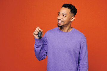 Poster - Young happy man of African American ethnicity in purple sweatshirt casual clothes hold car key fob keyless system look aside isolated on plain red orange background studio portrait Lifestyle concept