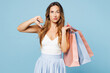 © ViDi Studio - Young sad woman wear casual clothes hold in hand paper package bags after shopping showing thumb down dislike gesture isolated on plain light pastel blue background. Black Friday sale buy day concept.