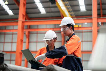 two men in orange and blue safety gear are looking at a laptop. they are likely discussing work or a