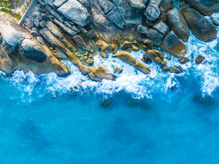 Bird's-eye view of rocky coastline with crashing waves and clear turquoise water in a tropical paradise during midday sun