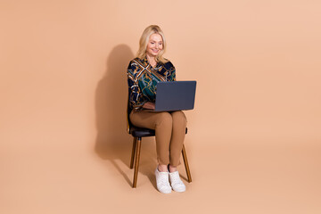 Wall Mural - Photo portrait of blonde mature age business woman sitting comfortable chair with laptop working sending email isolated on beige color background