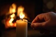 © Natalia - A close-up of a hand lighting a candle with a match, set against a warm and cozy background featuring a glowing fireplace
