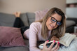 © BokishaNS - Beautiful woman wearing glasses reading book lying on couch. Attractive woman read funny book and smiling indoor in apartment