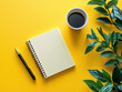 © Petzhy - flat lay of spiral bound notebook, pen, cup of coffee, and green plant on vibrant yellow background creates cheerful and inviting workspace