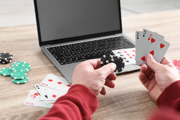 Canvas Print - Online poker. Man with playing cards, chips and laptop at wooden table indoors, closeup