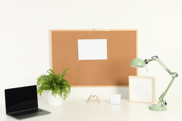 Sticker - Cork board with blank paper note, laptop, lamp and decorative elements on light table near white wall