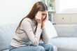 © KMPZZZ - Depressed anxiety asian young woman frustrated hand on head, touching her temples, suffering stressed, sick, tired, crisis on sofa from headache, migraine pain tension problem health care concept.