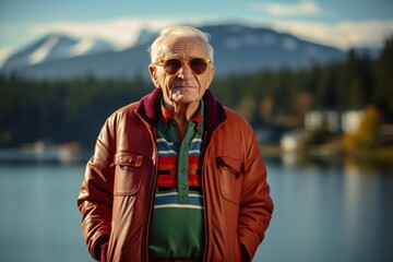 Wall Mural - Portrait of a content man in his 80s sporting a stylish varsity jacket while standing against serene lakeside view