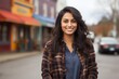 © Markus Schröder - Portrait of a satisfied indian woman in her 20s wearing a comfy flannel shirt isolated in charming small town main street