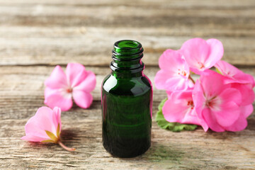 Canvas Print - Bottle of geranium essential oil and beautiful flowers on wooden table, closeup