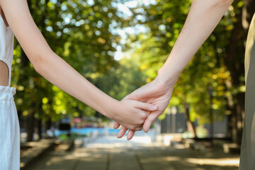 Wall Mural - Mother and daughter holding hands in park, closeup