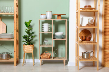 Wall Mural - Wooden storage stands and shelving unit with kitchenware near green wall indoors