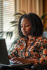 Wall Mural - A woman sits in a chair using a laptop computer, perfect for illustrations of remote work or technology-related concepts