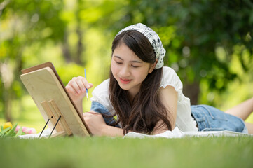 Young Asian woman artist painting with watercolor palette on paper using easel