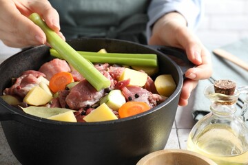 Poster - Woman preparing stew with vegetables and meat at white tiled table, closeup