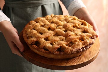 Sticker - Woman holding wooden board with tasty homemade apple pie on light background, closeup