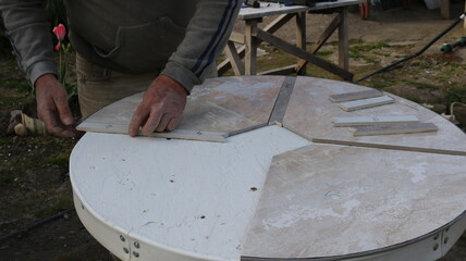 laying out pieces of ceramic tiles on the surface of a round tabletop to form a pattern for decorating a table, a tiler works with the material in the process of creating exclusive furniture