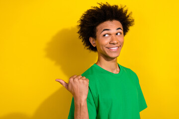 Poster - Photo of cheerful positive guy dressed green t-shirt pointing thumb emtpy space isolated yellow color background