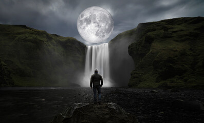 Wall Mural - man observes the full moon from the big waterfall
