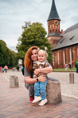 Wall Mural - A little Caucasian toddler girl with a young mother travels in Kaliningrad near the Cathedral in the city center.